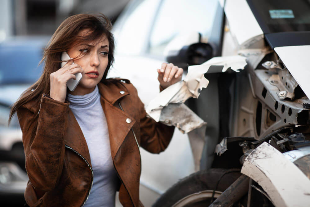 Eine besorgte Frau telefoniert neben einem beschädigten Auto nach einem unverschuldeten Unfall