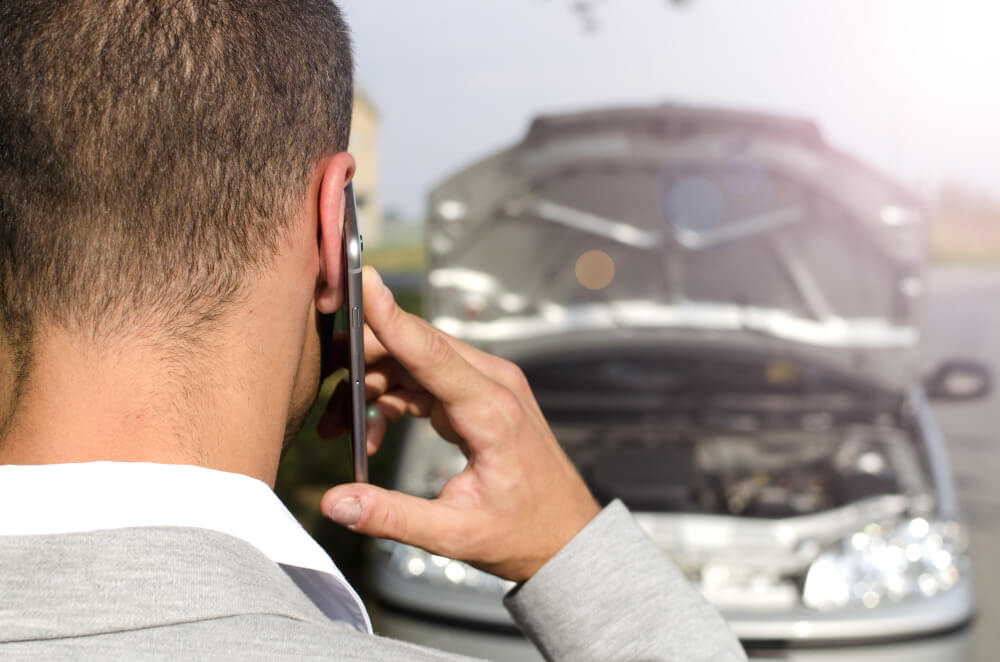 Ein Mann telefoniert neben einem Auto mit offener Motorhaube, vermutlich ruft er nach einem Haftpflichtschaden einen unabhängigen Gutachter