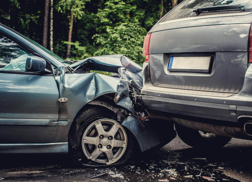 Ein silbernes Auto mit zerbeulter Motorhaube nach Auffahrunfall auf grauen SUV, Bäume im Hintergrund, automatisch gespeicherter Entwurf