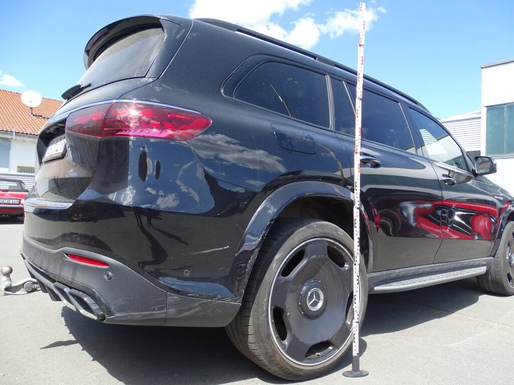 Ein schwarzer Mercedes-Benz SUV steht draußen in der Sonne, neben dem Hinterrad ist ein Messstab aufgestellt