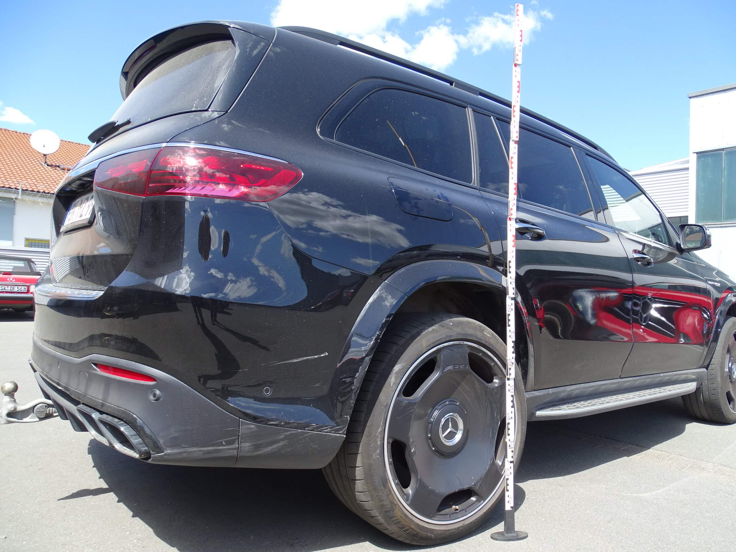 Ein schwarzer Mercedes-Benz SUV steht draußen in der Sonne, neben dem Hinterrad ist ein Messstab aufgestellt