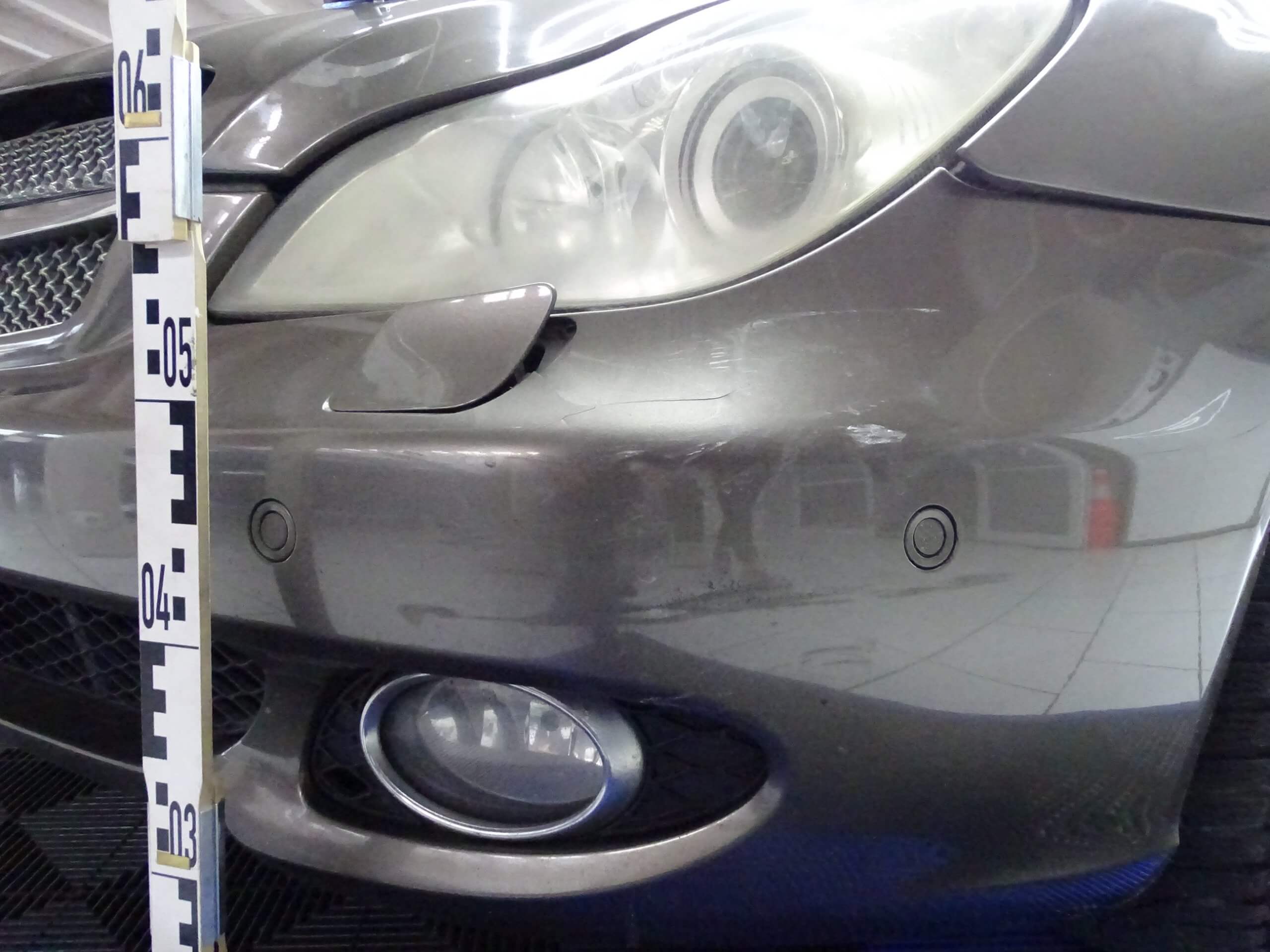 Frontstoßfänger eines Autos mit Kratzern, Scheinwerfer, Nebelscheinwerfer und Messskala zur Schadengutachten-Dokumentation