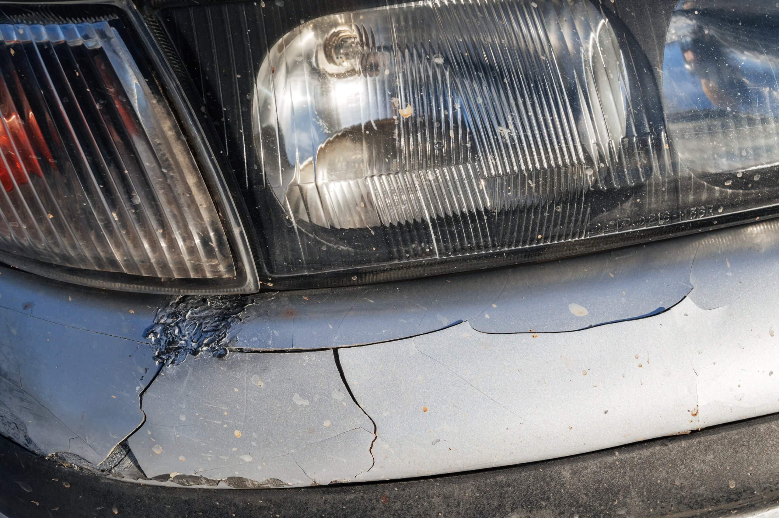 Nahaufnahme einer beschädigten vorderen Stoßstange eines Autos mit Riss unter dem Scheinwerfer, als Automatisch gespeicherter Entwurf markiert