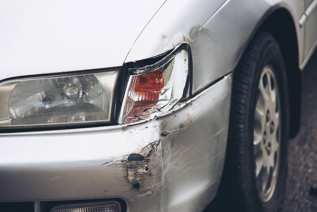 Nahaufnahme eines silbernen Autos mit automatisch gespeichertem Entwurf, der Schäden und Kratzer an vorderer Stoßstange und Scheinwerfer zeigt