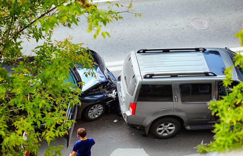 Ein dunkles Auto ist in einem grauen SUV auf einer Stadtstraße aufgefahren, daneben steht ein automatisch gespeicherter Entwurf unter grünen Ästen